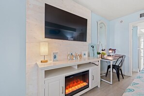 Ein Wohnzimmer mit Kamin, einem an der Wand befestigten Fernseher, einem Esstisch mit Stühlen und einem Spiegel.