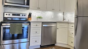 A modern kitchen with stainless steel appliances, white cabinetry, and a tiled backsplash.