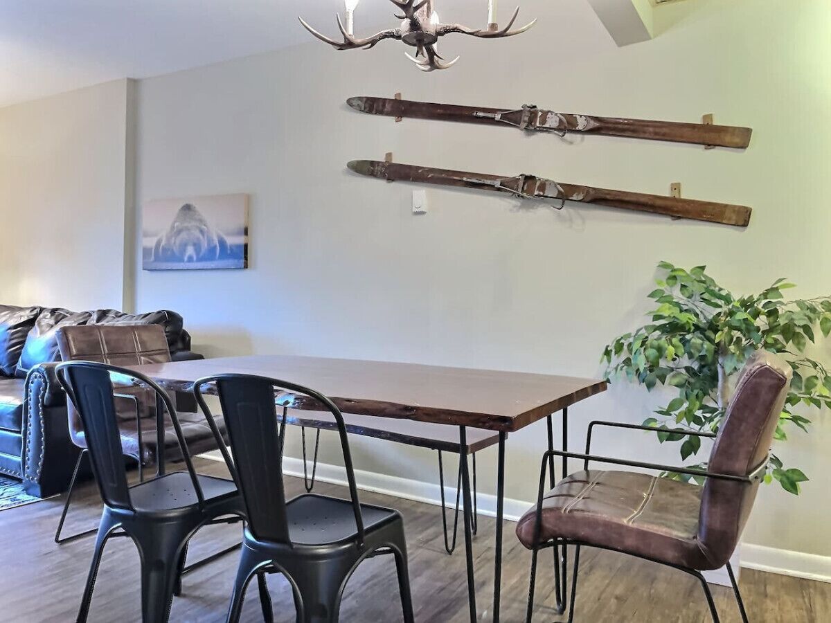 Uma sala de jantar com mesa de madeira e cadeiras de metal, um candelabro e um par de esquis fixados na parede.