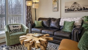 A cozy living room with a leather sofa, a wooden coffee table, and a green armchair with a pillow labeled 'SKI LODGE'.