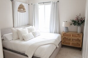 Restful retreat with a large bed, wicker pendant light, and a bedside table.