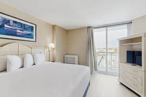 Ein Hotelzimmer mit einem großen Bett, einem Fernseher, einem Schreibtisch und einem Fenster mit Blick auf die Stadt.