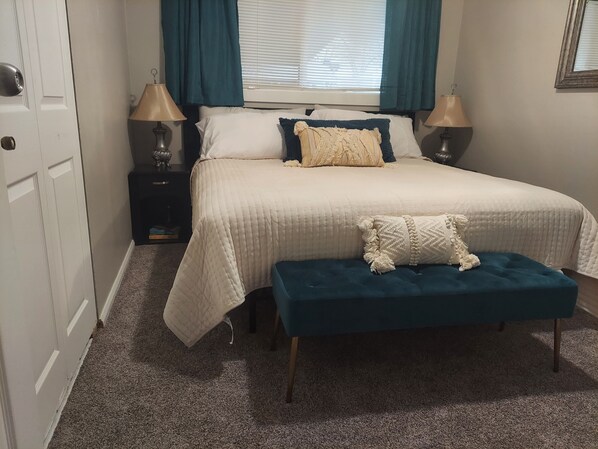 A bedroom with a bed, two bedside lamps, a window with curtains, a door, and a carpeted floor. - Cheerful 3 bedroom house. Great location near Broadmoor and the Cheyenne Mt. Zoo (Colorado Springs)