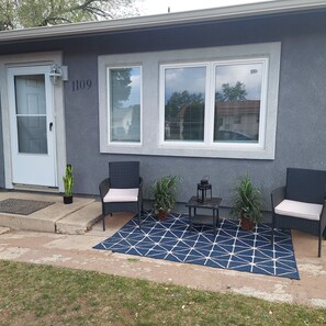 A house with a gray exterior, a white door, and a blue patterned rug. There are two wicker chairs with cushions and two potted plants. - Cheerful 3 bedroom house. Great location near Broadmoor and the Cheyenne Mt. Zoo (Colorado Springs)