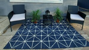 A patio area with two wicker chairs, a small table, and two potted plants.