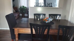 A dining area with a wooden table and black chairs. There is a window with curtains and a ceiling fan above the table.