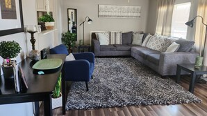 A living room with a sectional sofa, a blue armchair, a patterned rug, and a ceiling fan.