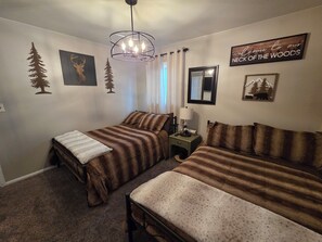 A bedroom with two beds, a nightstand, a lamp, and wall decorations including a 'Welcome to our Neck of the Woods' sign. - Cheerful 3 bedroom house. Great location near Broadmoor and the Cheyenne Mt. Zoo (Colorado Springs)