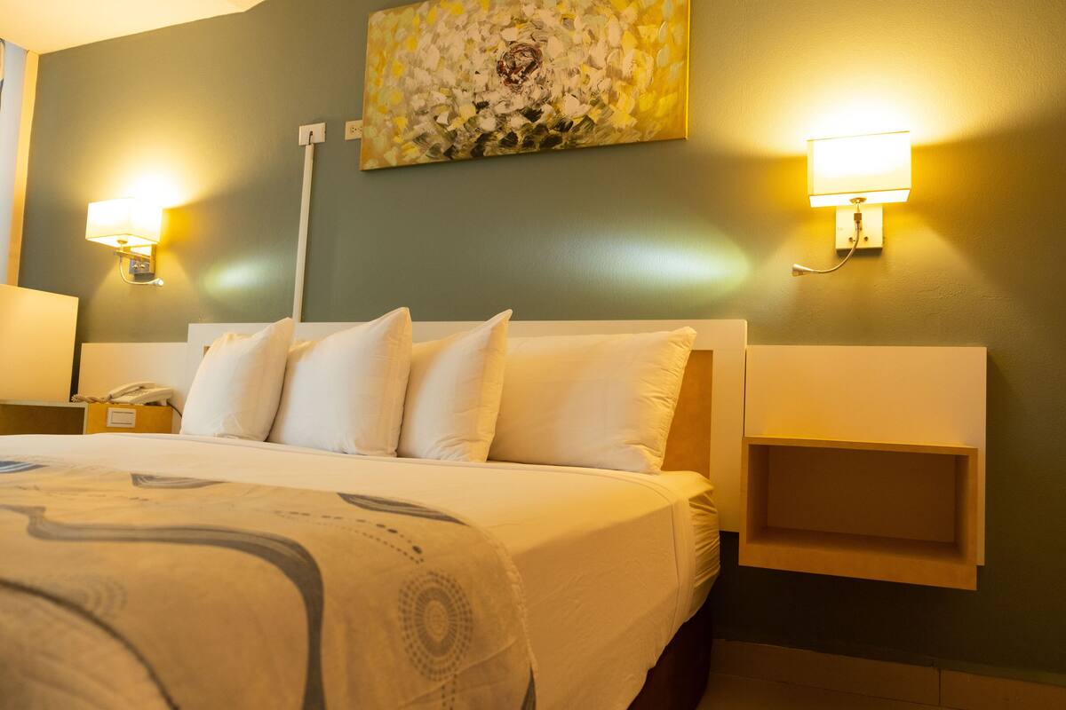 Ein Hotelzimmer mit einem großen Bett, zwei Nachttischen, einer Wandleuchte und einem Gemälde über dem Bett.