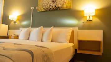 A hotel room with a large bed, two bedside tables, a wall-mounted light, and a painting above the bed.