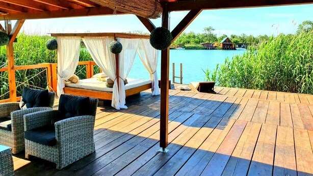 A wooden deck with wicker furniture and a canopy bed overlooking a body of water. - Ivana Houses Ada Bojana (Ulcinj)