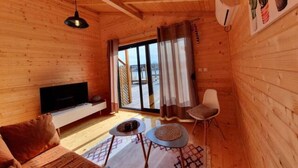 A wooden cabin interior with a sofa, a TV, a chair, and a small table. - Ivana Houses Ada Bojana (Ulcinj)