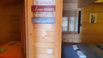 A wooden cabin with two beds, one with a green blanket and the other with a blue blanket. There is a sign on the wall with various phrases about love and memories.