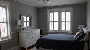 Un dormitorio con cama, cómoda y dos ventanas.