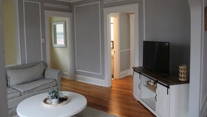 Una sala de estar con un sofá gris, una mesa de centro blanca, un televisor de pantalla plana sobre un mueble de madera y un ventilador de techo.