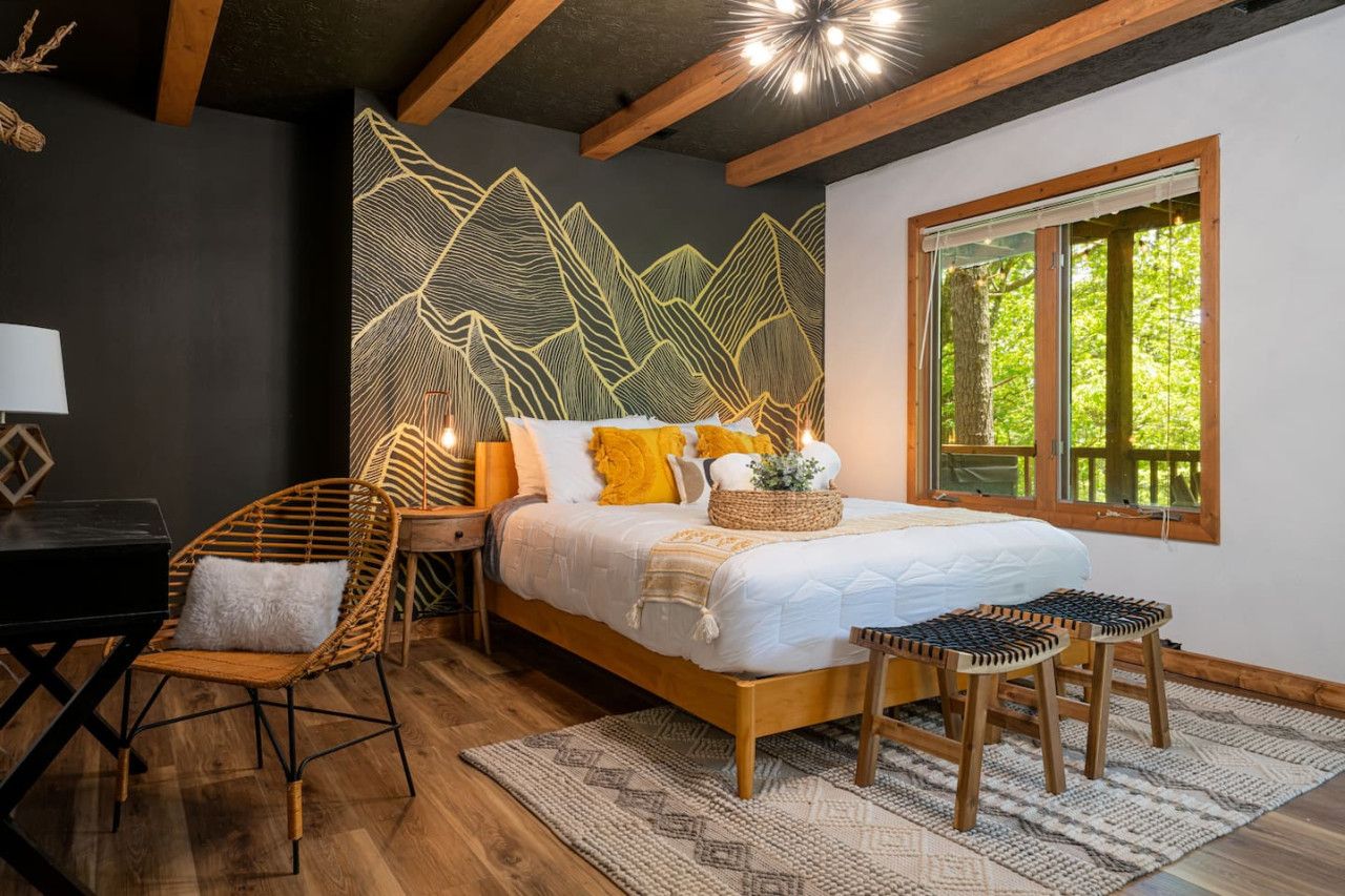 Ein Schlafzimmer mit einem Bett, einem Schreibtisch, einem Sessel und einem Fenster mit Blick auf Bäume.