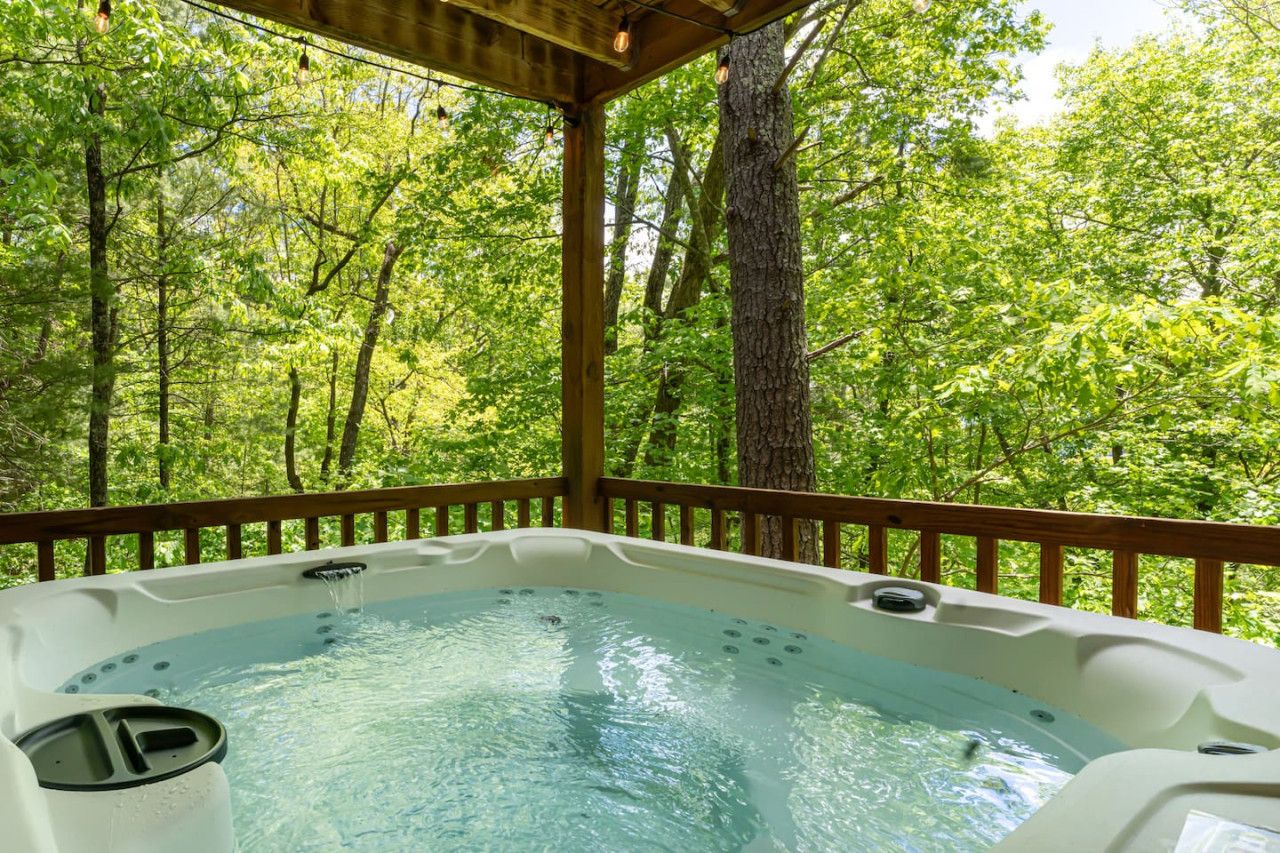 A hot tub surrounded by a wooden deck with a forest view.