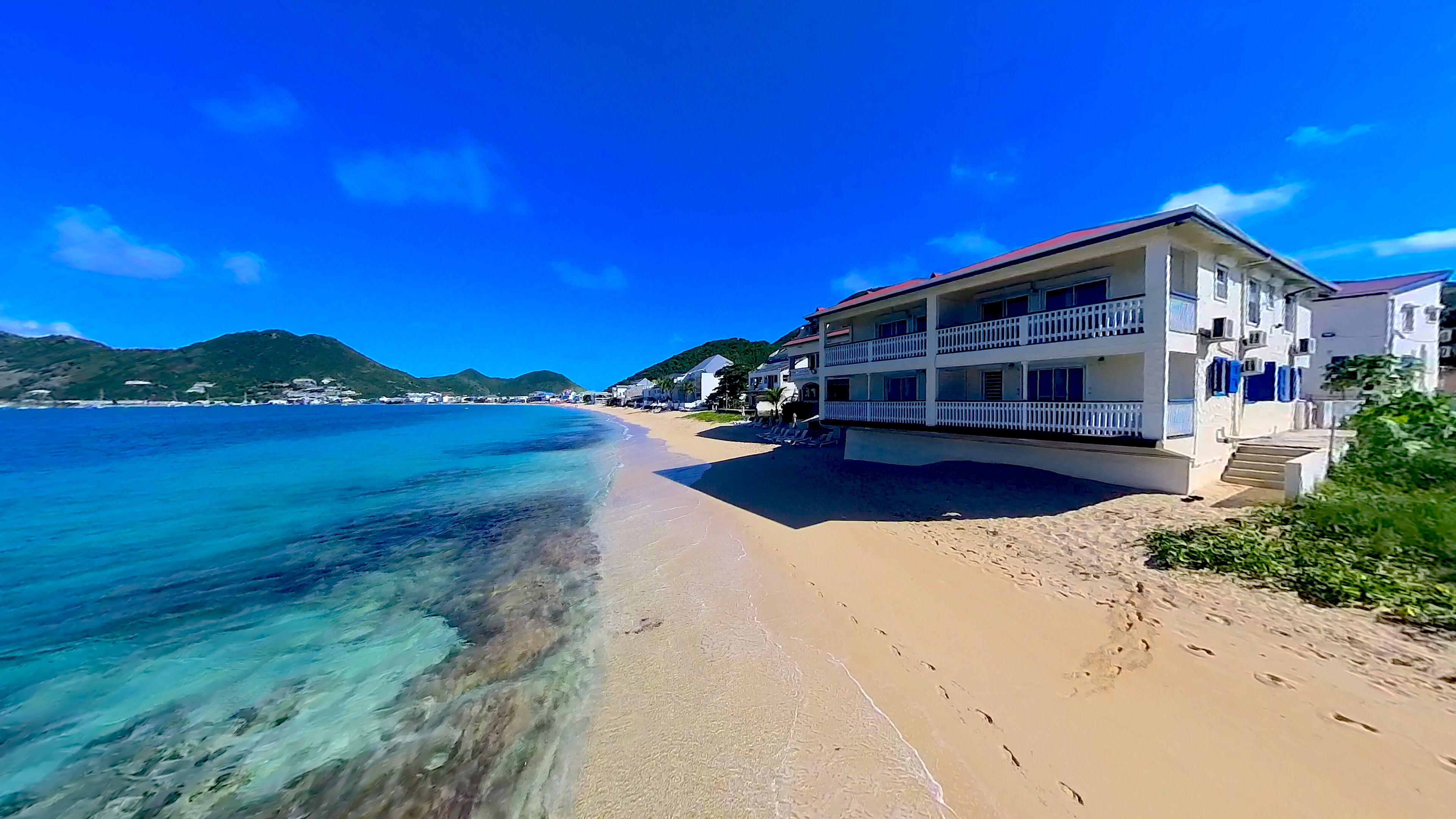 A beachfront hotel with a balcony, clear blue water, and a mountain in the background.