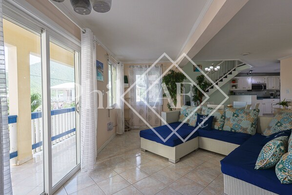 A spacious living area with a large sofa, a staircase, and a kitchen in the background. - Spacieux Duplex at Gd Case (Grand-Case)