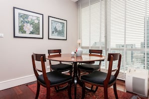 A dining area with a round table, four chairs, two framed floral paintings, and a window with blinds. - 1 Bed Serviced Skyvilla With View - Check in From 15h to 22h Only (Bangkok)