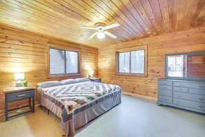 A wooden cabin bedroom with a bed, dresser, nightstands, and a ceiling fan.