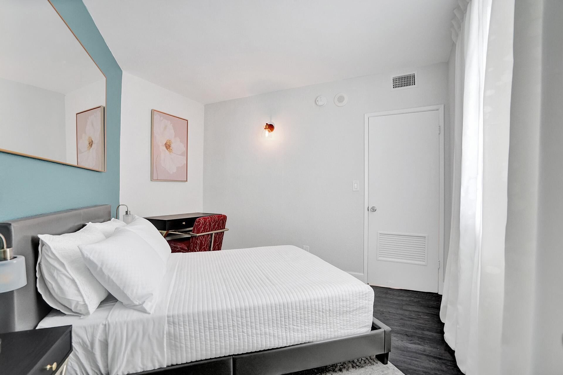 Un dormitorio moderno con una cama, una mesita de noche, un tocador, un espejo y una puerta.