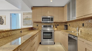 A modern kitchen with stainless steel appliances, granite countertops, and light wood cabinetry.
