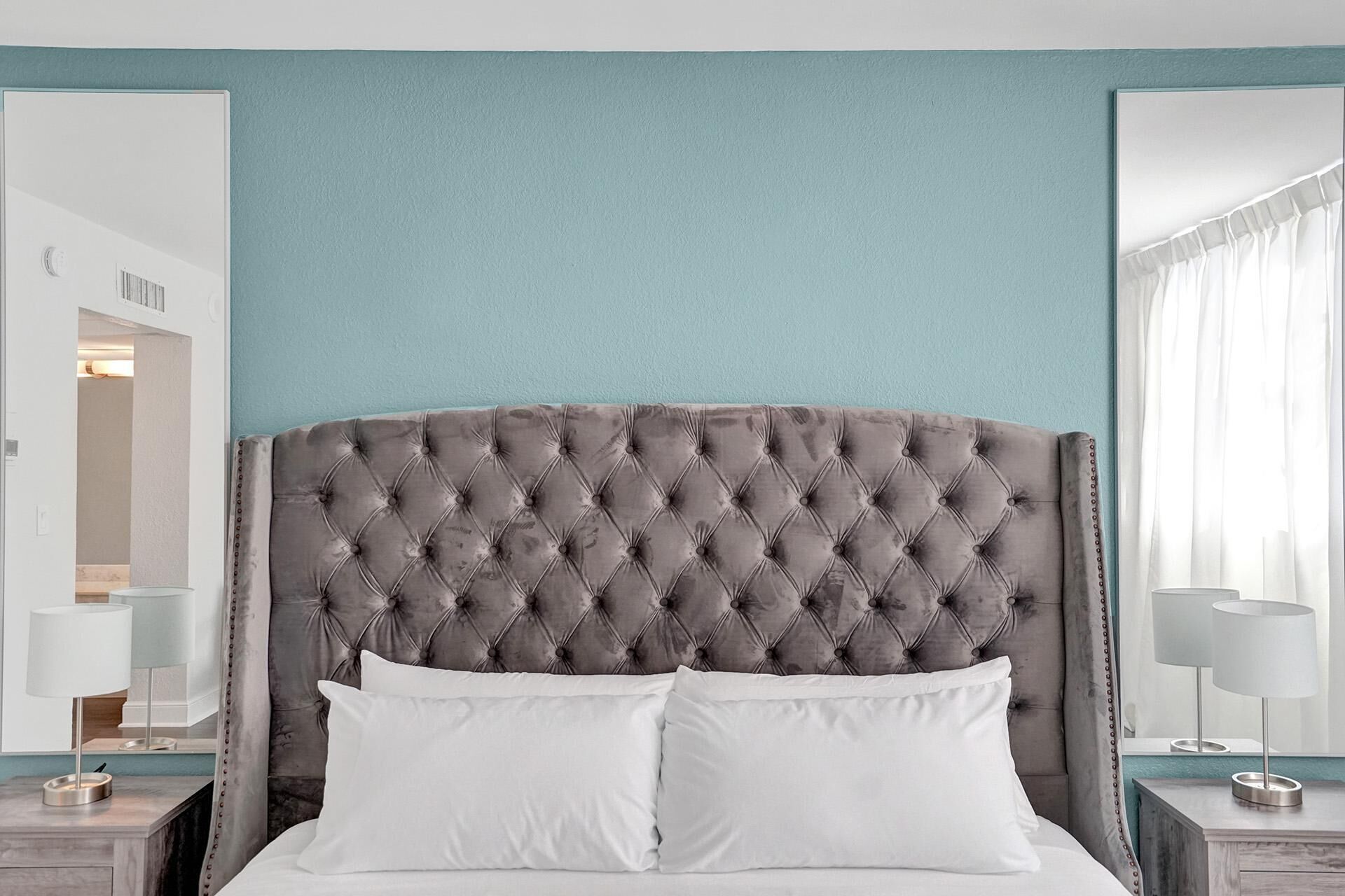 A bed with a tufted headboard, white pillows, and two bedside tables with lamps.