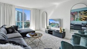 A modern living room with a grey sofa, a coffee table, a TV, and a large window with curtains.