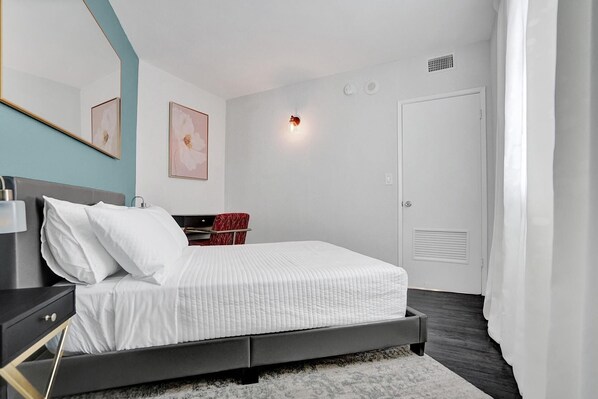 A modern bedroom with a bed, bedside table, and a desk with a chair.