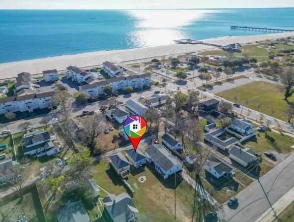 An aerial view of a coastal residential area with houses, a beach, and a pier.