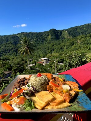 A colorful plate of food with a scenic mountain view in the background. - Le Petit Paradis (Roseau)