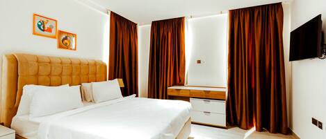 A modern hotel room with a large bed, a wooden nightstand, a dresser, a flat-screen TV, and two framed pictures on the wall.