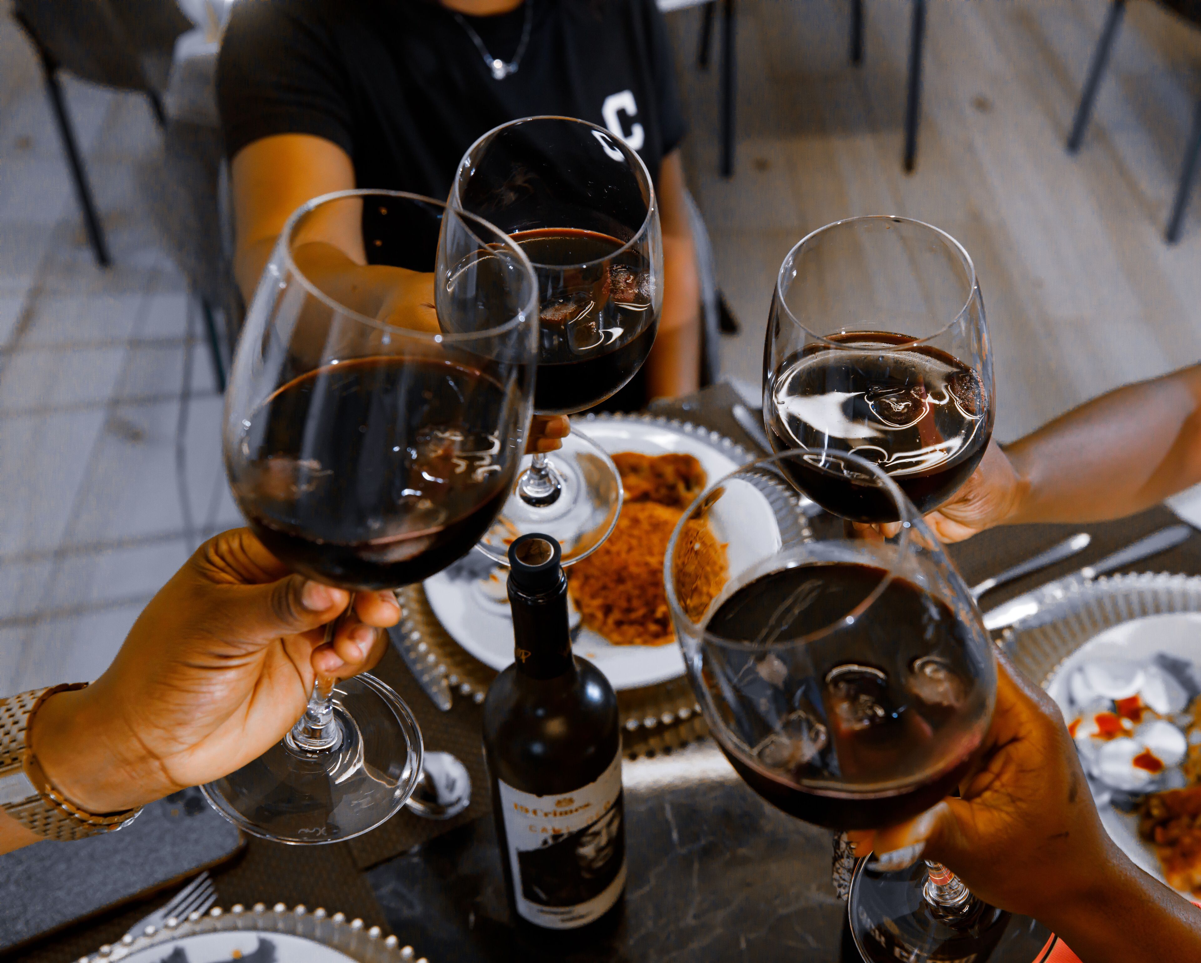 A group of people toasting with wine glasses at a table with a bottle of wine.