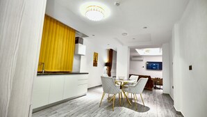 Een moderne keuken met witte kastjes, een geel raamkleed, en een eethoek met een witte tafel en stoelen.