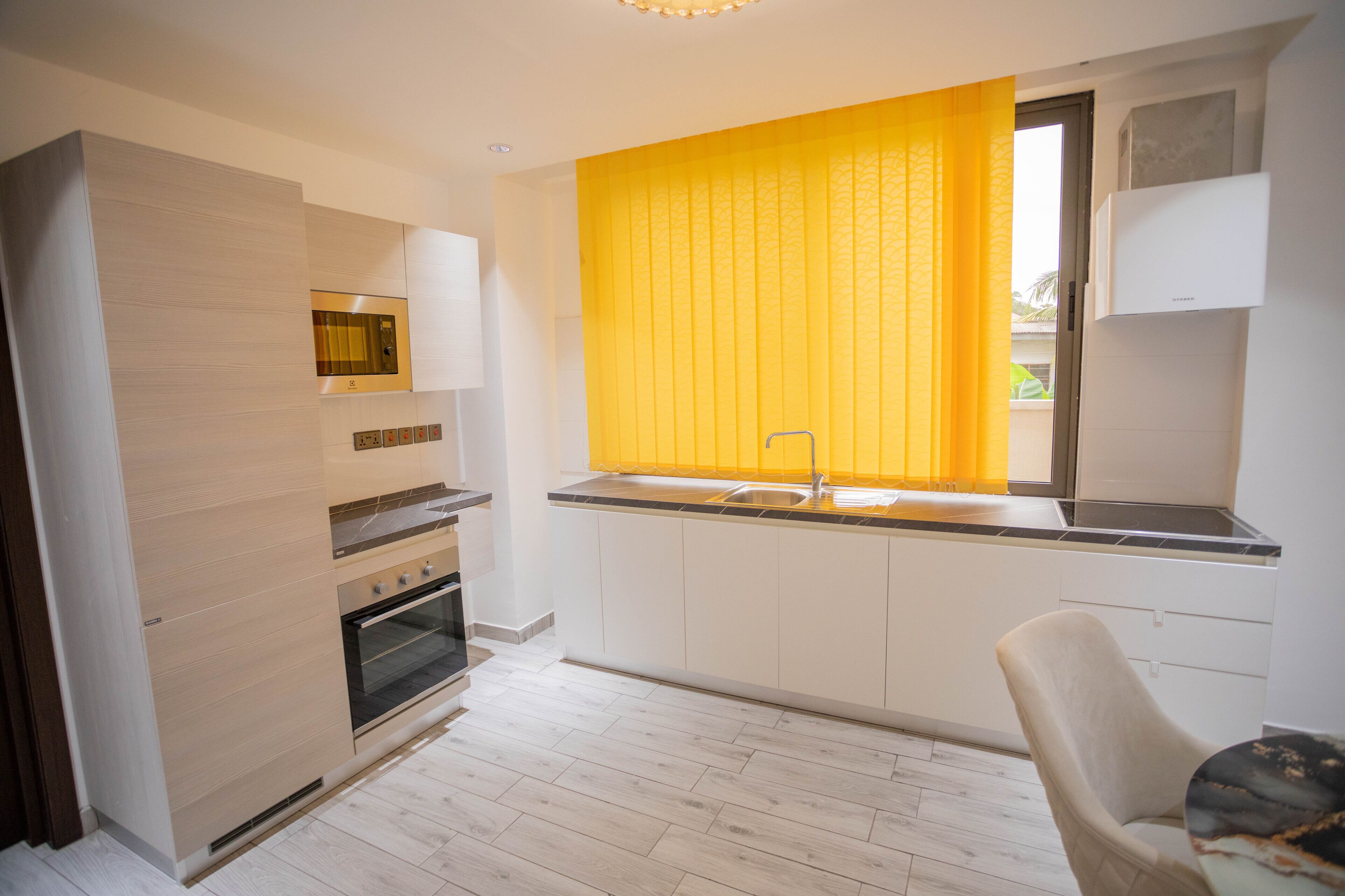 Una cocina moderna con armarios blancos, horno empotrado y una ventana con cortinas amarillas.