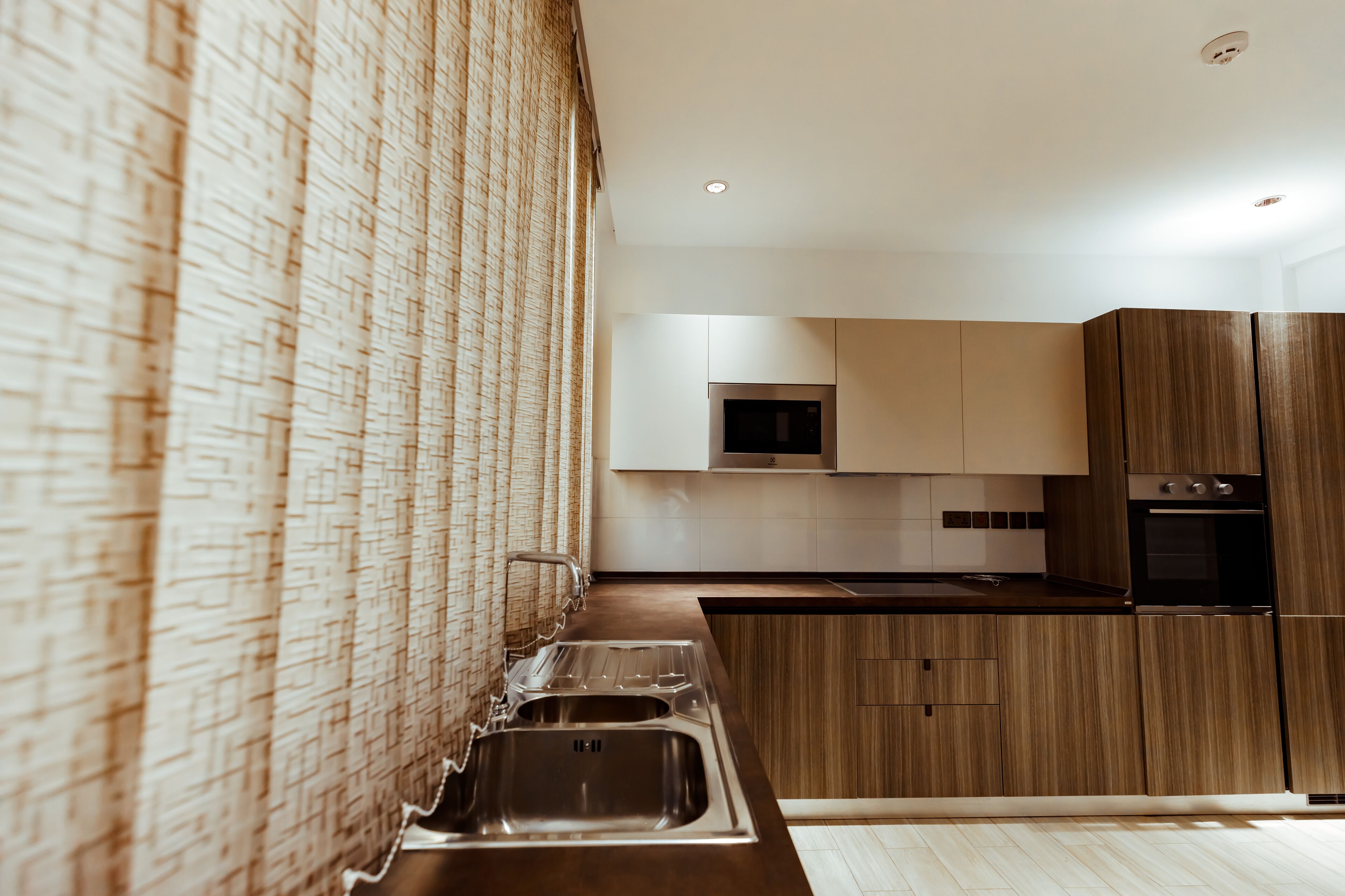 Una cocina moderna con un lavamanos de acero inoxidable, armarios de madera y un microondas.