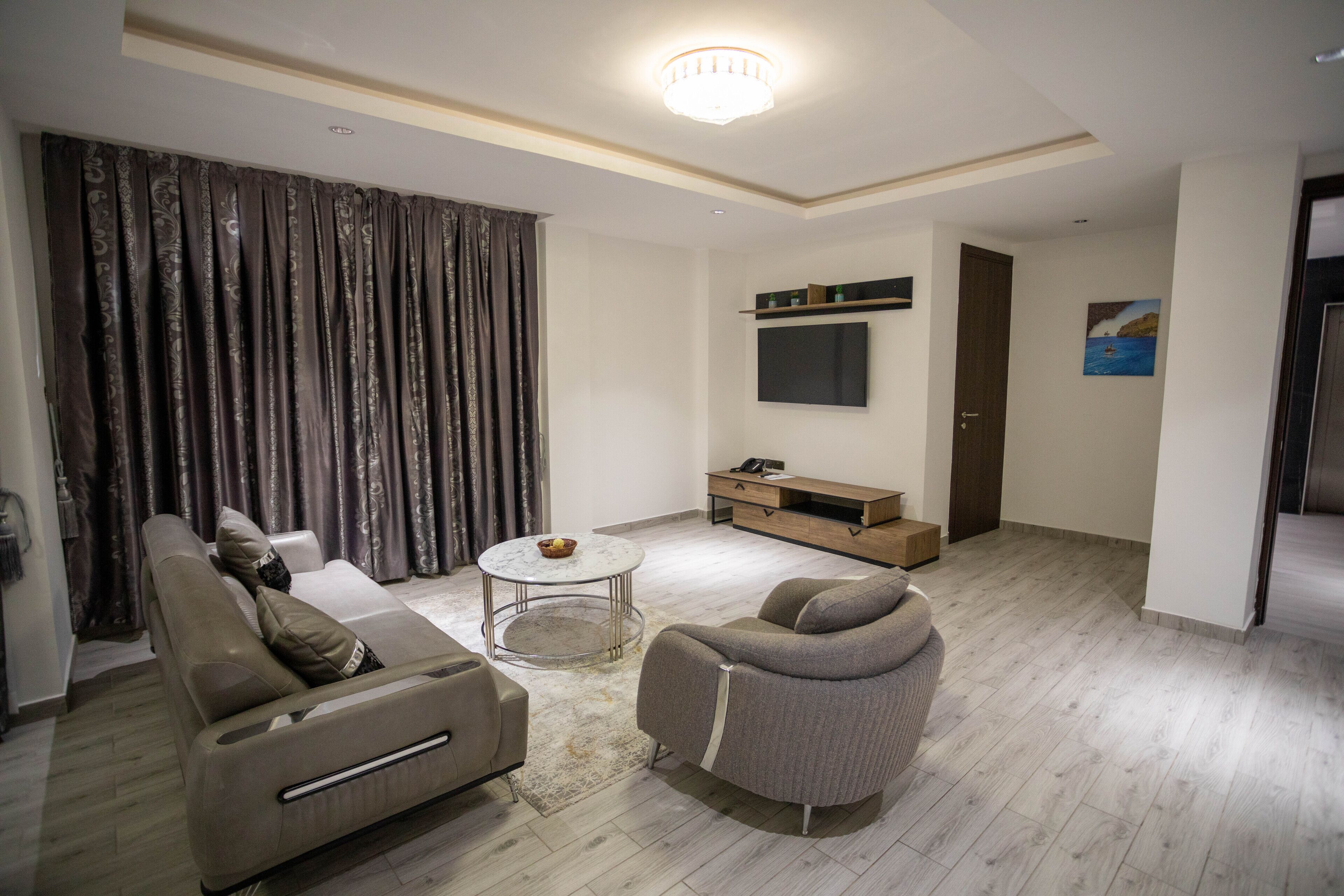 A modern living room with a sofa, armchair, coffee table, and a flat-screen TV mounted on the wall.