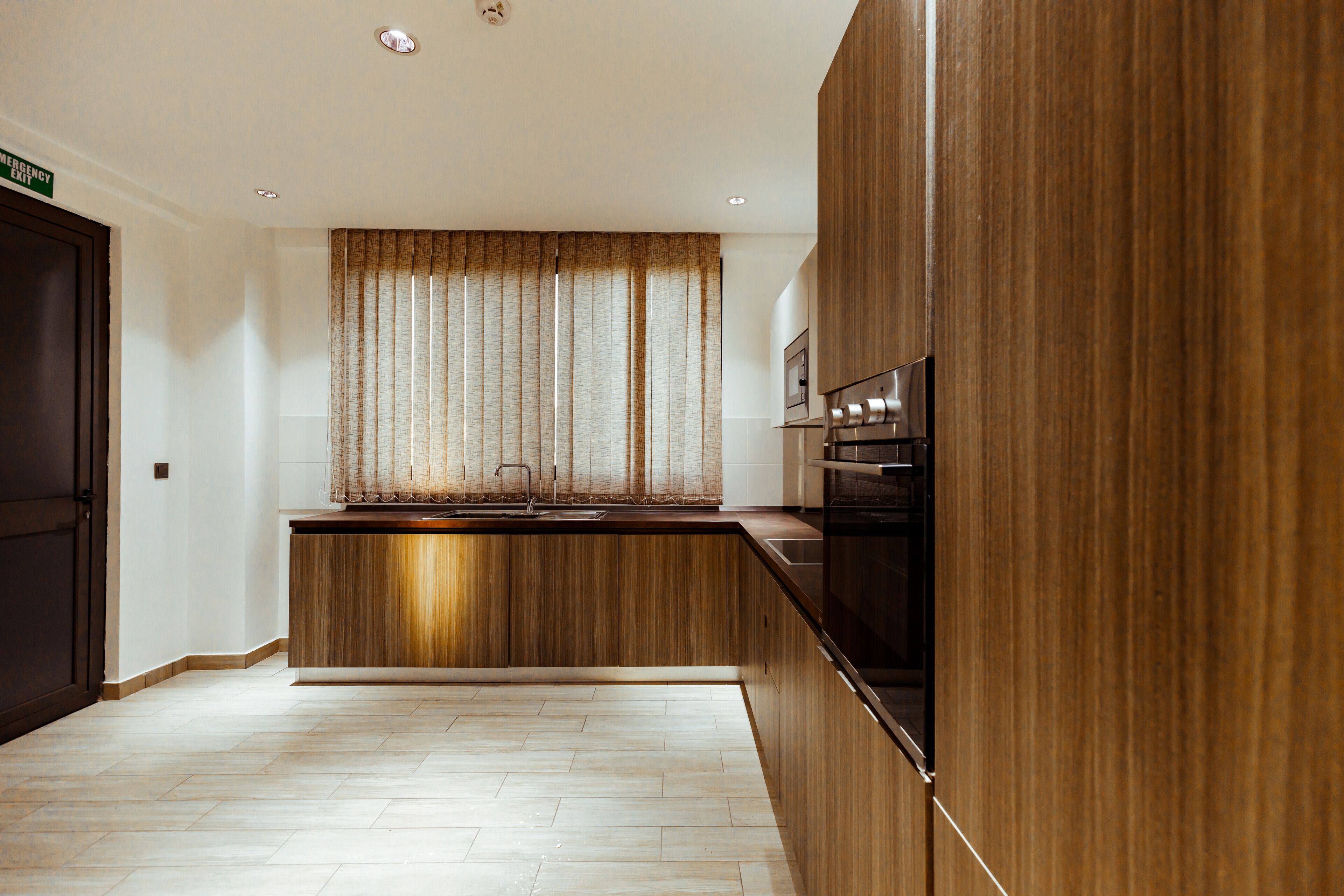 A modern kitchen with wooden cabinetry, a built-in oven, and a window with curtains.