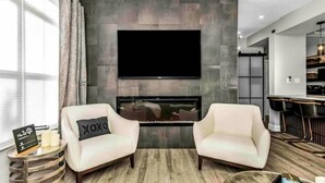 A modern living room with a fireplace, two white armchairs, a coffee table, and a flat-screen TV mounted on the wall. - Wonderful Avalon Condo (Ground Floor) - Renovated & Steps to Pool!!!🏝️ (Clearwater)
