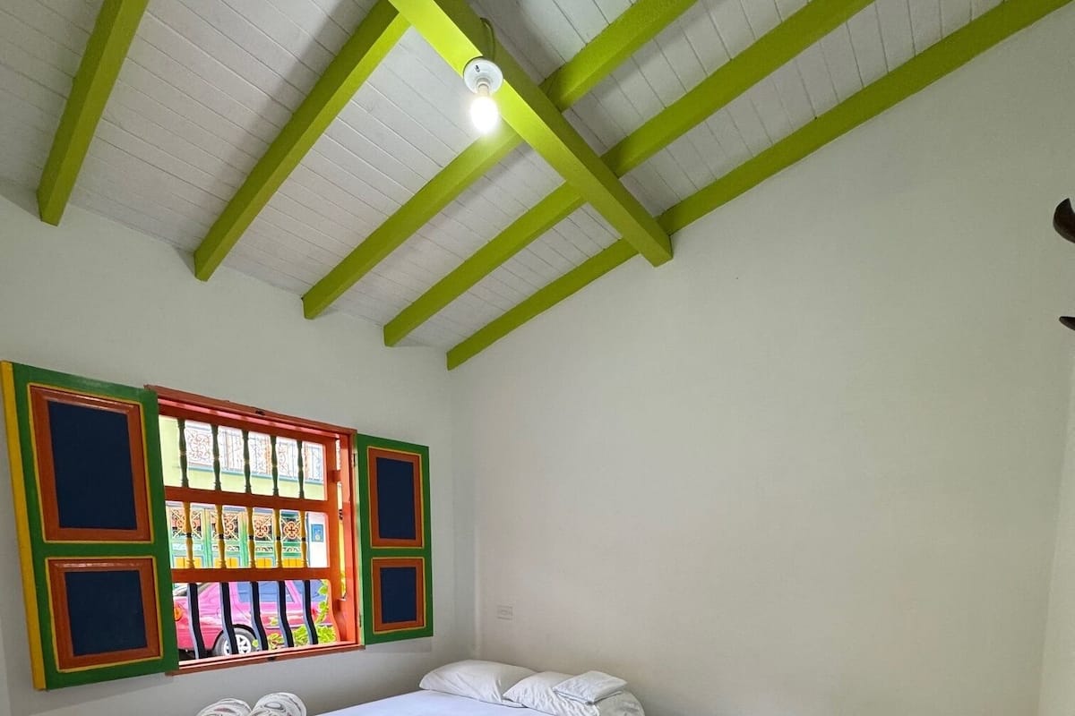 A room with two beds, a window with colorful frames, and a ceiling with green beams.