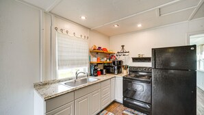A kitchen with white cabinets, a black refrigerator, a stove, and a microwave. - Cozy Canyon Lake Cottage Rental w/ Private Hot Tub (Canyon Lake)