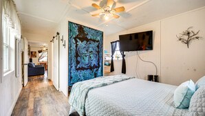 A bedroom with a bed, a ceiling fan, a TV mounted on the wall, and a large floral tapestry. - Cozy Canyon Lake Cottage Rental w/ Private Hot Tub (Canyon Lake)