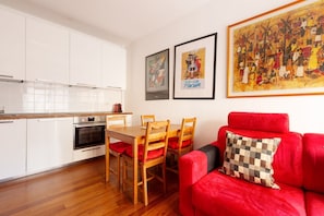 Una cocina moderna con armarios blancos, una mesa de comedor de madera con cojines rojos y un sofá rojo con un cojín a cuadros.