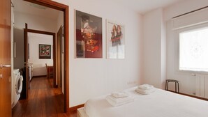 Quarto com cama, máquina de lavar e corredor que leva a um banheiro.