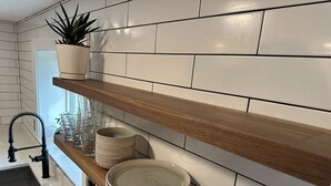 Une cuisine avec des murs recouverts de carreaux blancs, des étagères en bois, une plante en pot et un robinet moderne.