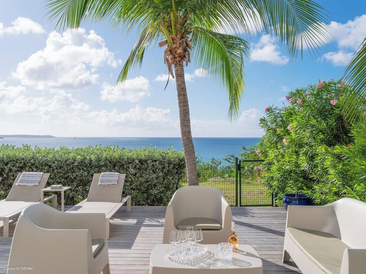 A deck with lounge chairs and a table, overlooking the sea.