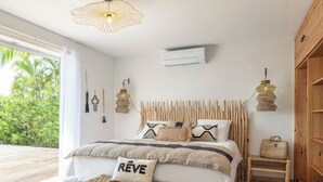 Une chambre à coucher avec un lit, une table de chevet, un banc et une vue sur la verdure à l’extérieur.