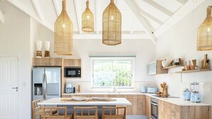 Une cuisine moderne dotée d’un îlot central, de chaises en bois et de luminaires suspendus en osier.