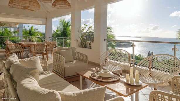 Un grand espace extérieur aménagé avec des meubles en osier, une table en bois et une vue sur la mer.